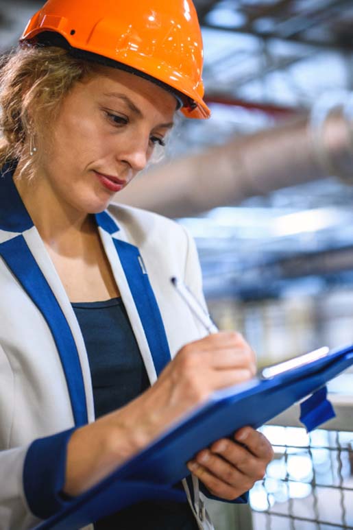 Facility Managerin bei einer Objektbegehung mit Helm und Klemmbrett